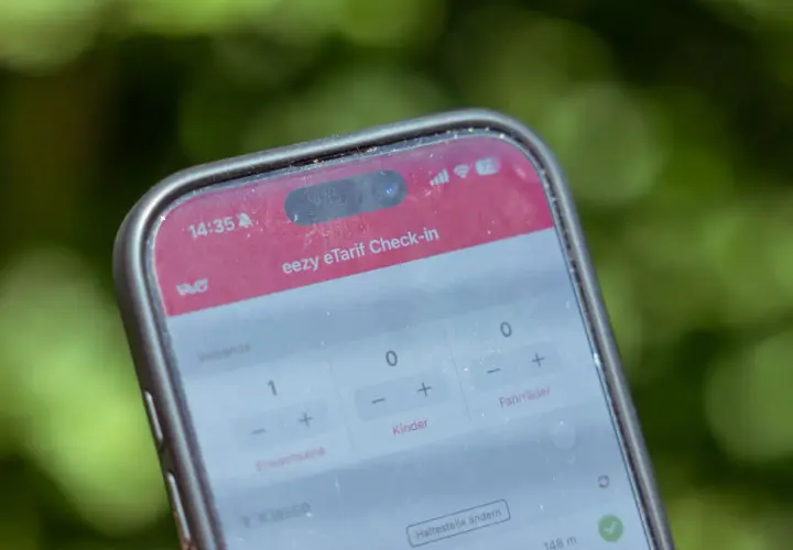 Ein Smartphone zeigt die "eezy eTarif Check-in" App. Ein Erwachsener und ein Kind sind für die Fahrt ausgewählt.