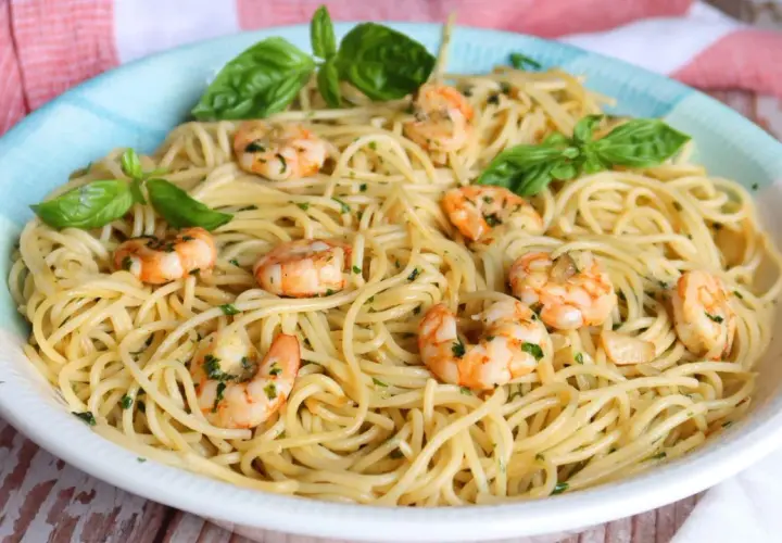 Un plato de espaguetis con gambas, adornado con hojas de albahaca fresca y perejil picado.