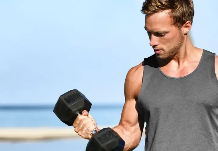 Mężczyzna ćwiczy biceps na świeżym powietrzu, podnosząc ciężarek. Zastanawia się, ile serii na biceps wykonać dzisiaj.