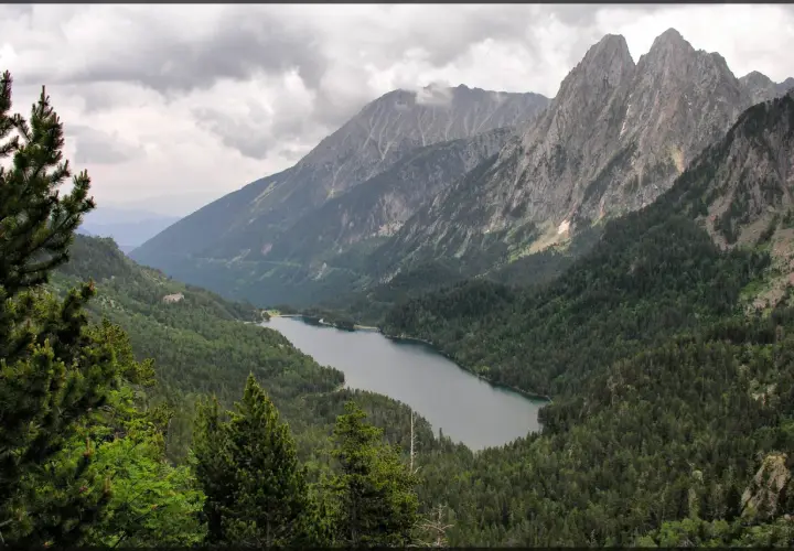 Paisaje montañoso con un lago sereno rodeado de bosques frondosos, ideal para explorar rutas desde Espot.