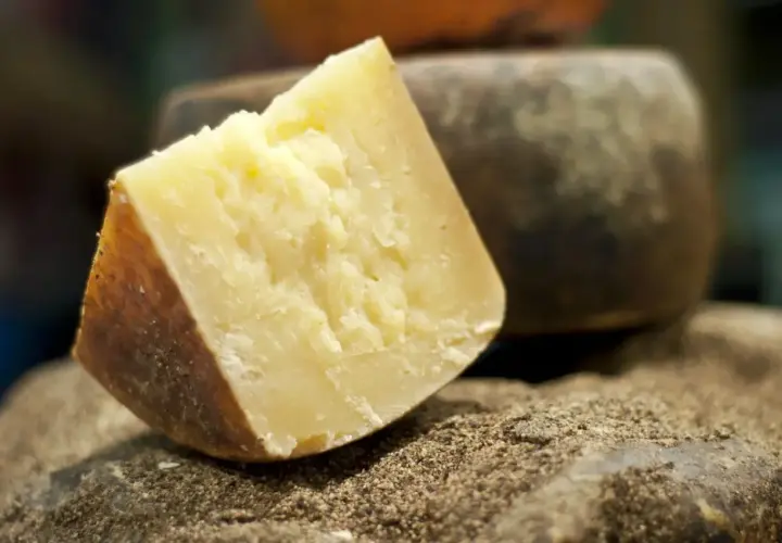 Kawałek twardego, żółtego sera, idealnego do pesto, leży na kamieniu obsypanym pieprzem.