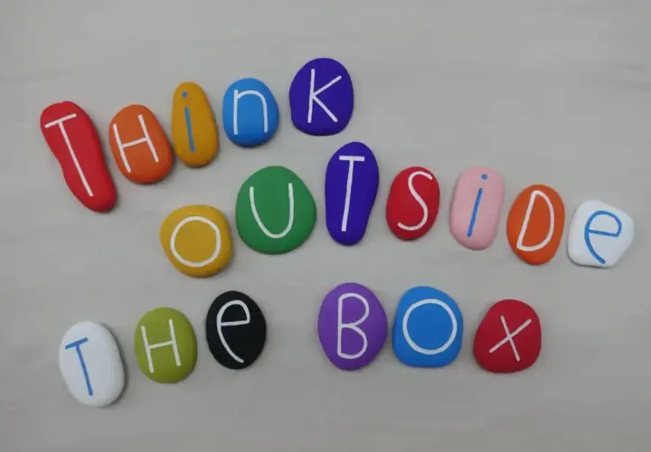 Kolorowe kamienie z literami tworzą napis "THINK OUTSIDE THE BOX". To jak polskie przysłowia po angielsku, zachęcające do nieszablonowego myślenia.