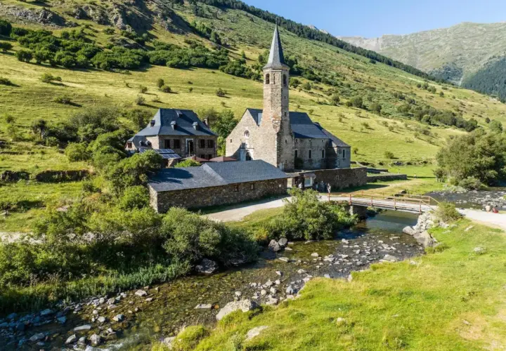 El santuari de Montgarri, una joya arquitectónica de piedra, se alza sereno junto a un arroyo cristalino, rodeado de verdes laderas montañosas.