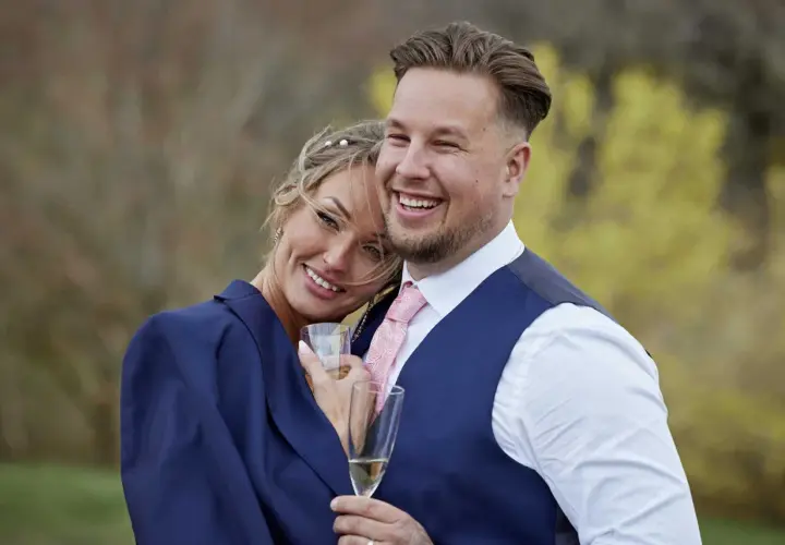 Ett lyckligt par, som från Love is Blind, firar med champagne. Rasmus ler stort, hans partner lutar sig mot honom.