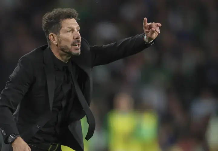 Cholo, trener Atletico Madryt, w czarnym garniturze gestykuluje na boisku, wskazując coś swoim zawodnikom.