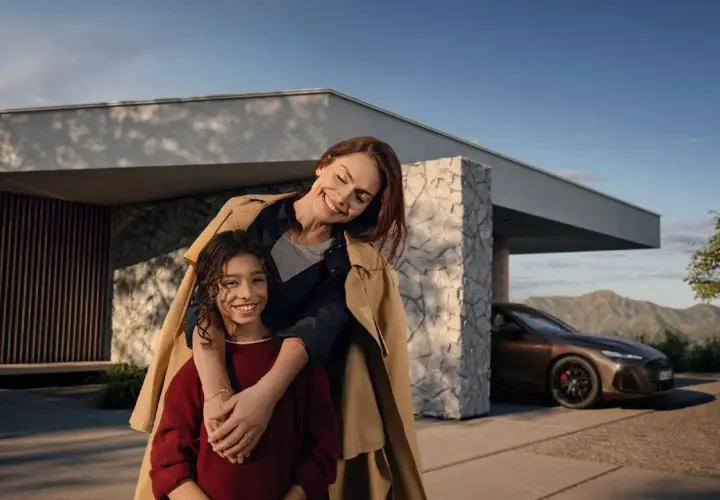 Madre e hija sonríen frente a una casa moderna con un Mercedes. El mantenimiento de tu Mercedes es clave para estos momentos.