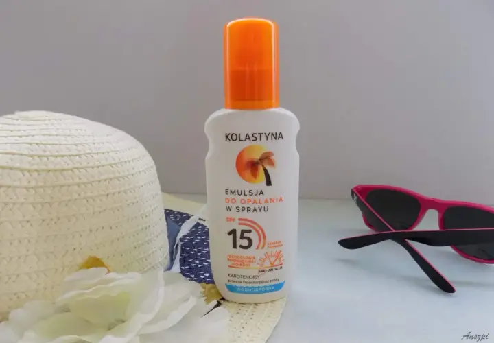 Emulsja do opalania w sprayu Kolastyna SPF 15 z karotenoidami, wodoodporna. Obok kapelusz i okulary przeciwsłoneczne.