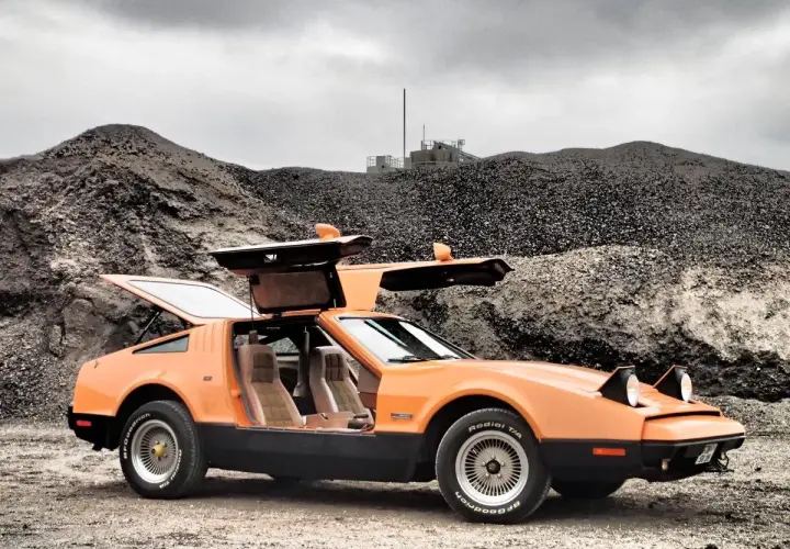 Orange Bricklin SV1 mit Flügeltüren steht auf Schotter vor einer Kiesgrube.
