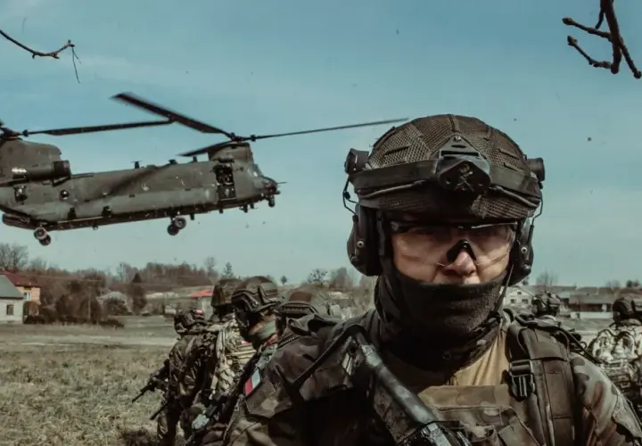 Żołnierze w pełnym rynsztunku, gotowi do akcji podczas szkolenia wojskowego. W tle widać helikopter transportowy.