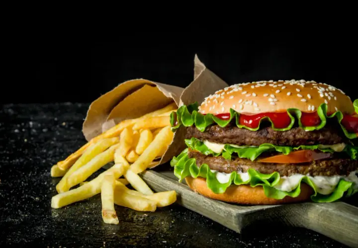 Podwójny hamburger z frytkami na ciemnym tle.