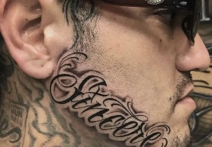 Wyrazisty tatuaż na twarzy z napisem "Sincere" w ozdobnej czcionce.