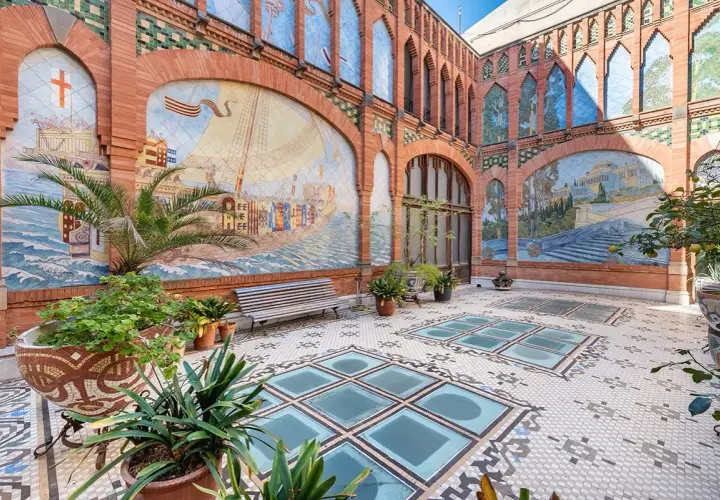 Patio de la Casa Navàs de Reus, con murales cerámicos que narran historias marítimas y paisajes, suelo de mosaico y plantas.