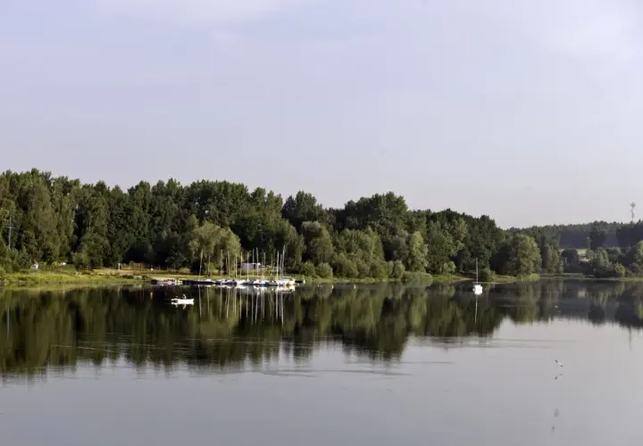 Spokojne jezioro Przeczyckie z odbijającymi się w wodzie drzewami i żaglówkami przy brzegu.