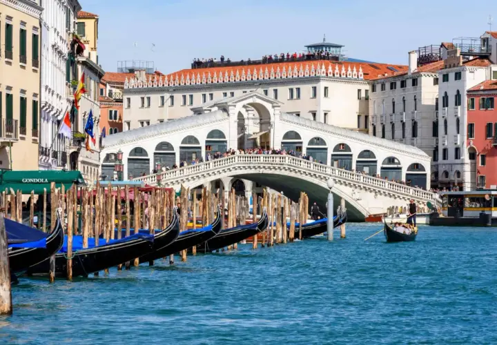 Gondoles amarrées près du célèbre Ponte di Rialto, avec des touristes admirant la vue sur le Grand Canal.