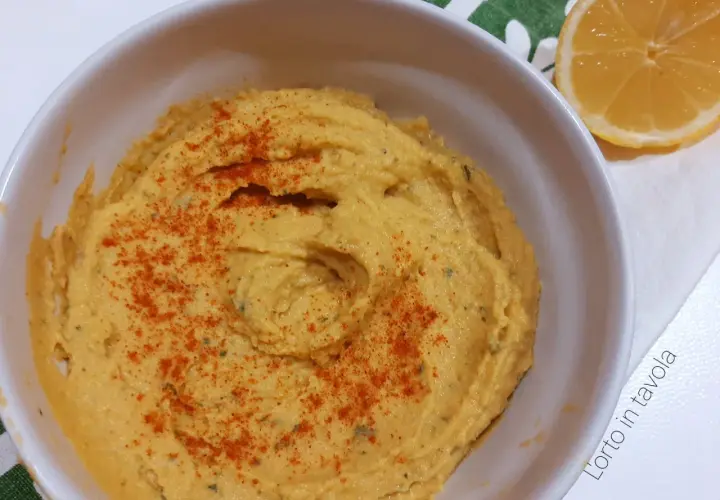 Hummus di ceci senza tahina, cremoso e spolverato di paprika, pronto per essere gustato con una fetta di limone.