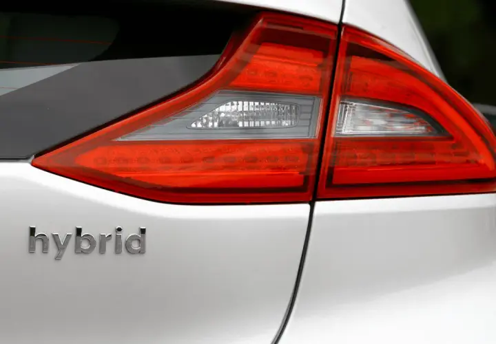 Detalle de la parte trasera de un coche blanco con la palabra "hybrid" en relieve. Las luces traseras rojas y blancas son visibles.