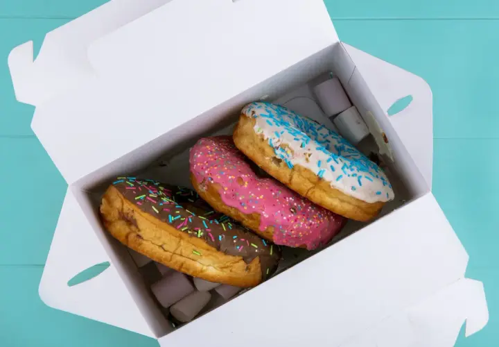 Pyszne opakowanie cukiernicze z trzema kolorowymi donutami: czekoladowym, różowym i białym z niebieską posypką.
