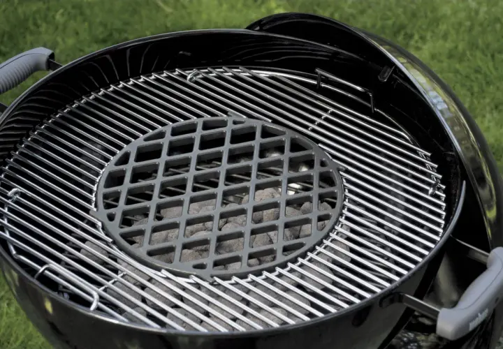 Grill ogrodowy z rusztem i węglem drzewnym.