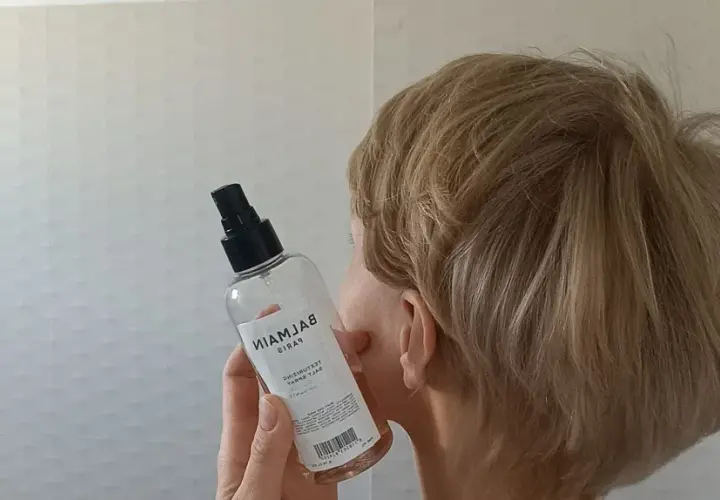 Kobieta z blond włosami trzyma butelkę z atomizerem, która zawiera sól morską do stylizacji włosów.