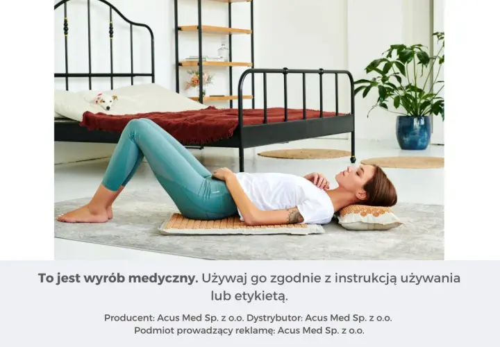 Kobieta leży na macie akupresurowej, która zapewnia masaż uda. W tle łóżko z psem.