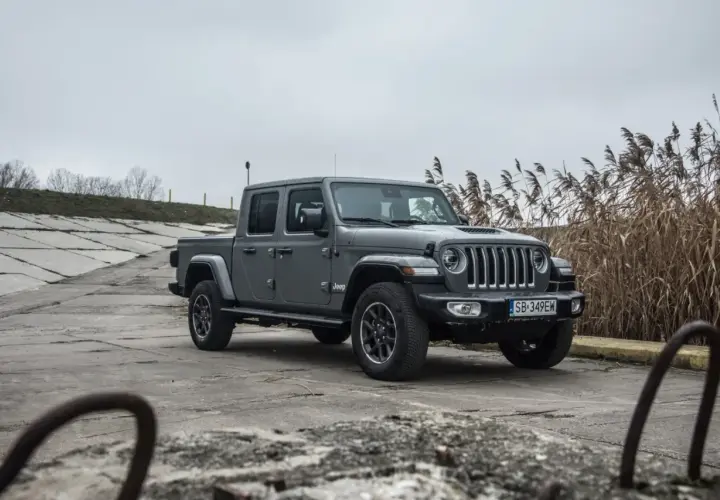 Szary Jeep Gladiator na betonowym podłożu, z suchymi trawami w tle.