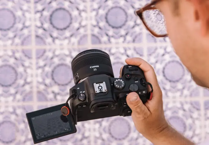 Osoba trzyma aparat Canon R6 z obiektywem 35mm, testując jego możliwości na tle wzorzystej ściany.
