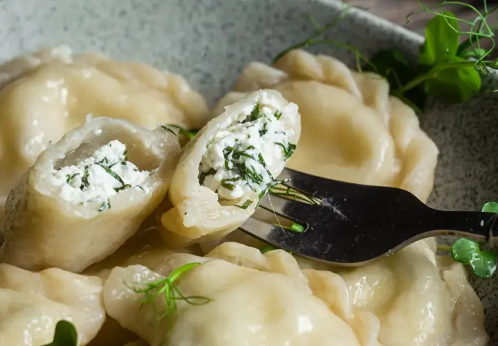 Pyszne pierogi z serem i zieloną natką, jeden uchwycony widelcem, gotowy do skosztowania.