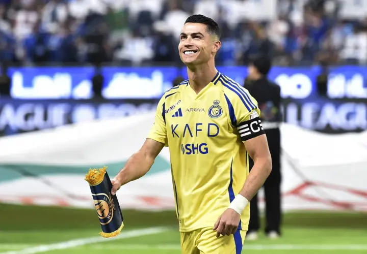 Uśmiechnięty Cristiano Ronaldo w żółtej koszulce Al Nassr, trzymający zwinięty szalik. Jego ogromne cristiano ronaldo zarobki budzą podziw.
