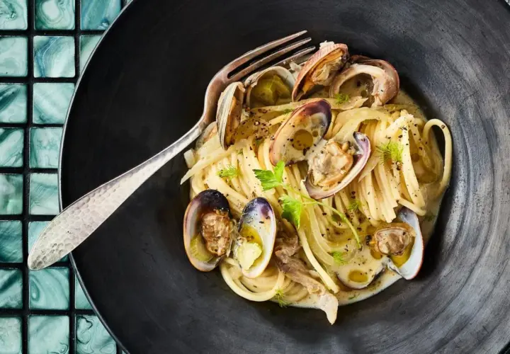 Spaghetti mit Venusmuscheln, ein köstliches Rezept. Serviert in einer schwarzen Schüssel mit einer Gabel.