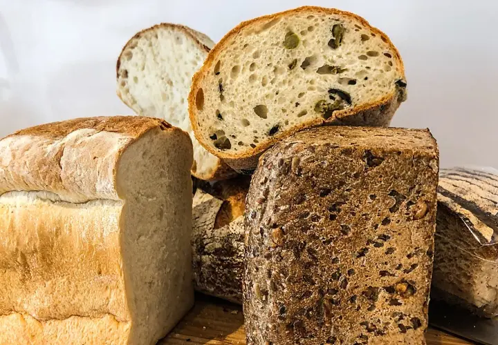 Variedad de panes artesanales, incluyendo un pan blanco esponjoso, un pan con aceitunas y un pan proteico con semillas.
