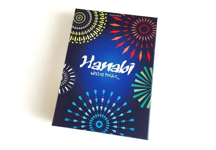 Pudełko gry karcianej Hanabi z kolorowymi fajerwerkami na ciemnoniebieskim tle.