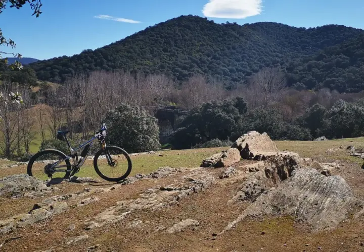 Bicicleta de montaña lista para explorar las **rutas en bici de montaña** en un paisaje rocoso y boscoso bajo un cielo azul.