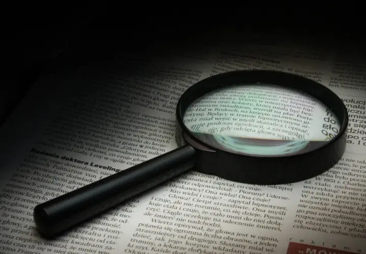 Lupa powiększa tekst, symbolizując dociekliwość i spostrzegawczość – kluczowe cechy dobrego detektywa.