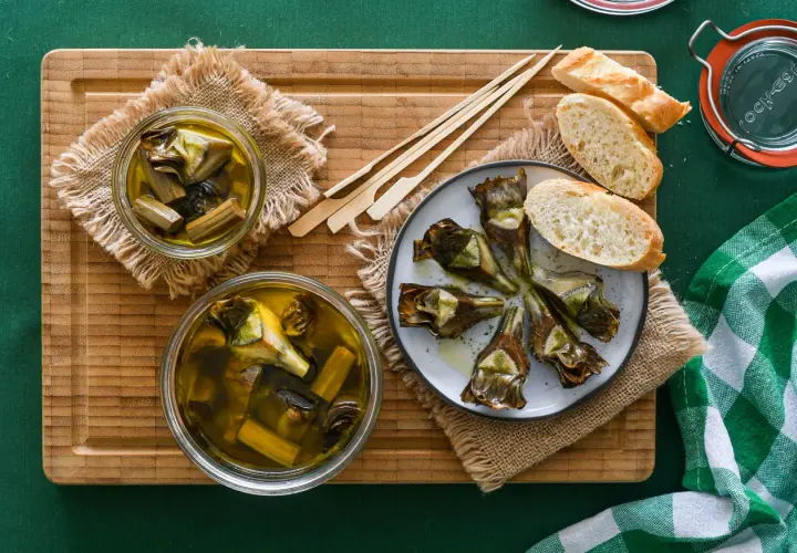 Deliciosas alcachofas confitadas en aceite de oliva, servidas con pan y palillos. Un manjar listo para disfrutar.
