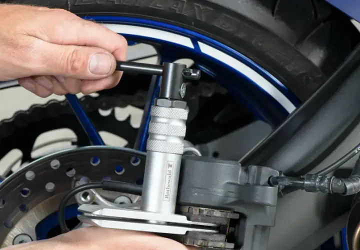 Wymiana klocków hamulcowych w motocyklu: narzędzie do cofania tłoczków zacisku hamulcowego ułatwia pracę przy tylnym kole.