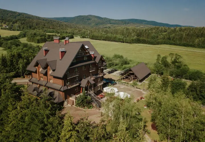 Hotel Carpatia Bieszczadzki Gościniec w otoczeniu zieleni, z drewnianym budynkiem i widokiem na góry.