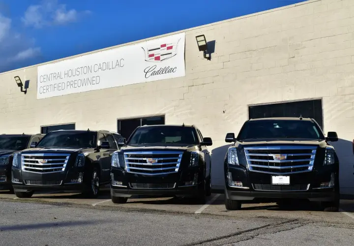 Trzy czarne Cadillac Escalade zaparkowane przed budynkiem salonu samochodowego.