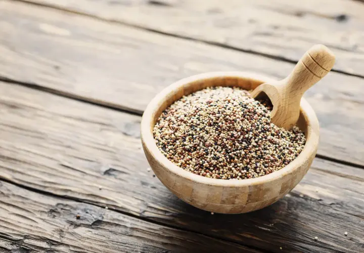 Ciotola di legno piena di quinoa tricolore, un legume nutriente, con un mestolo di legno.