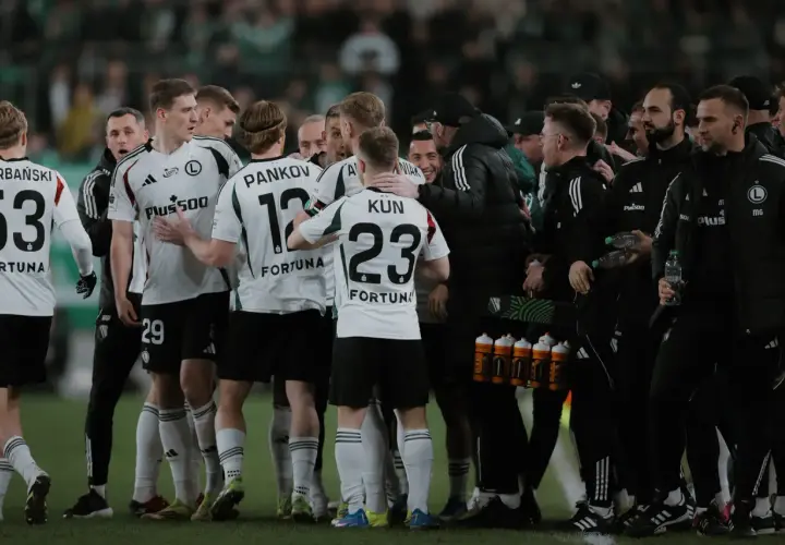 Legia Warszawa zawodnicy w białych strojach świętują na boisku. Widać numery 53, 29, 12 i 23.