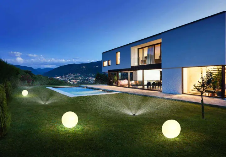 Modern villa con piscina iluminada y aspersores automáticos, un ejemplo de ideas domotica para un jardín perfecto.