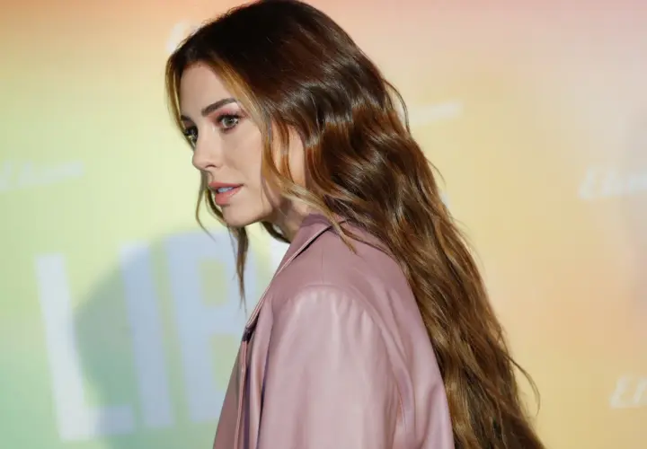 Mujer con cabello largo y ondulado, de color de pelo avellana con reflejos dorados, luciendo un traje rosa.
