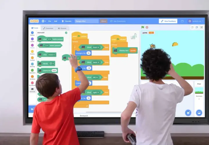 Zwei Kinder lernen Programmieren an einer digitalen Tafel in der Schule. Sie erstellen ein Spiel mit Scratch, das auf einem micro:bit basiert.