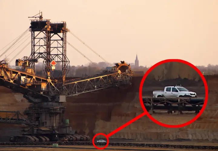Największa koparka świata w kopalni odkrywkowej. W oddali widać mały biały pickup, który wygląda jak zabawka przy gigantycznej maszynie.