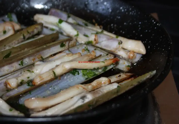 Longueirón de Fisterra cocinándose en una sartén con perejil picado. Un plato marinero listo para disfrutar.