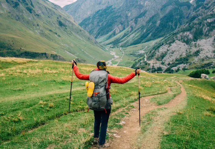 A hiker with a large backpack and trekking poles embraces the stunning alpine scenery on a self-guided tour du mont blanc.
