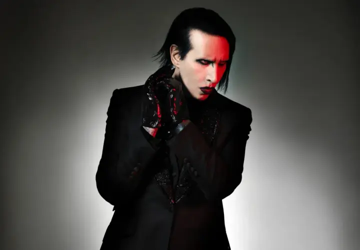 Marilyn Manson, wokalista zespołu, w czarnym garniturze i błyszczących rękawiczkach, z czerwonym światłem na twarzy.