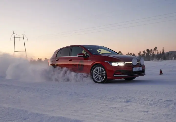 Czerwony Golf podczas kormoran snow test na zaśnieżonej drodze, z chmurą śniegu unoszącą się spod kół.