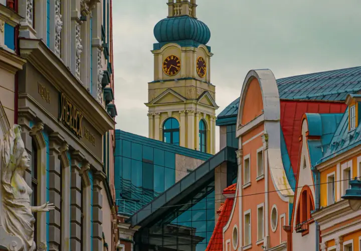 Architektura Rygi zachwyca. Zobaczysz tu zabytkowe kamienice i nowoczesne budynki, a w oddali wieżę zegarową.
