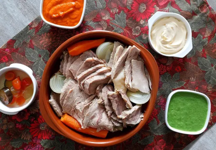 Un invitante bollito di carne, affettato e servito con carote, cipolle e tre salse: una rossa, una bianca e una verde.