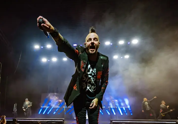 Wokalista Three Days Grace Polska z mikrofonem w dłoni, na scenie pełnej dymu i świateł.